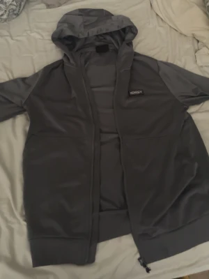 Mörkgrå hoodie med dragkedja - Säljer en mörkgrå hoodie med dragkedja och huva. Hoodien har en enkel och clean design med fickor framtill och ett litet tygmärke på bröstet. Perfekt för dig som gillar en avslappnad och stilren look.