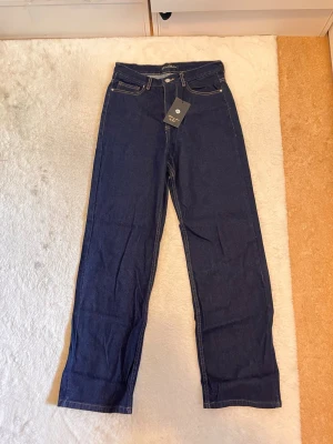 Mörkblå raka jeans med hög midja - Snygga mörkblå jeans med raka ben och hög midja. Klassisk femficksmodell med kontrastsömmar och dragkedja. Jeansen är i ett kraftigt denimtyg som ger en tidlös look och passar perfekt till olika stilar.