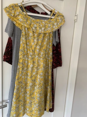 Gul blommig  klänning - Söt gul klänning med vitt blommönster. Klänningen har en volang runt axlarna och är tillverkad i ett lätt tyg, perfekt för varma dagar. Midjan är markerad för en feminin siluett.