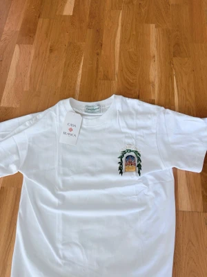 Vit t-shirt från Casablanca - Vit t-shirt från Casablanca med ett färgglatt broderat motiv på bröstet och rund hals. Tillverkad i mjuk bomull och har en klassisk passform. Perfekt för dig som gillar stilrena plagg med unika detaljer.