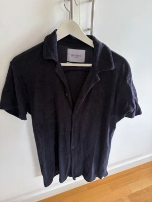 Mörkblå frottéskjorta Les Deux - Kortärmad skjorta från Les Deux i mörkblå frotté. Skjortan har klassisk krage, knappar framtill och en avslappnad passform. Perfekt för en chill och stilren look.