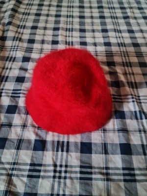Röd fluffig bucket hat - Cool röd bucket hat i fluffigt material som ger en trendig och lekfull look. Perfekt accessoar för att sticka ut och addera färg till din outfit. Hatten har en mjuk och rundad form med bredare brätte.