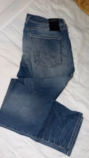 Blå raka jeans från Replay - Säljer ett par blå jeans från Replay med raka ben och klassisk femficksdesign. Jeansen har en snygg tvätt med lätt slitning och detaljerade sömmar på bakfickorna. Perfekta för en avslappnad och trendig look.