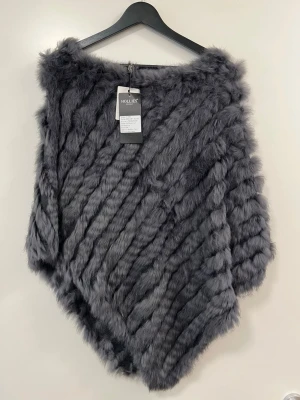 Antracitgrå poncho i kaninpäls Hollies - Snygg poncho från Hollies i antracitgrå kaninpäls och akrylstickning. Ponchon har en mjuk, fluffig känsla och ett diagonalt mönster som ger en exklusiv look. Perfekt för dig som vill ha något extra till höst- och vintergarderoben.