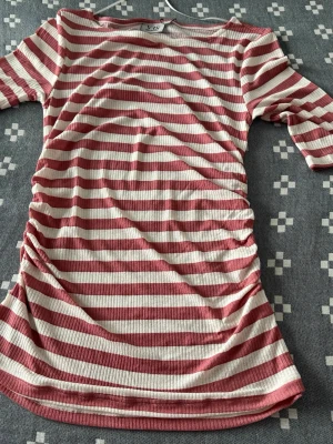 Randig ribbad topp med trekvartsärm - Säljer en ribbad topp med rosa och vita ränder. Toppen har trekvartsärm och är i ett mjukt, stretchigt material. Perfekt för dig som gillar en avslappnad men ändå trendig stil.