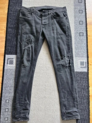 Dondup george - Säljer ett par svarta dondup george med slitningar och hål på benen för en trendig look. Jeansen har fem fickor och är tillverkade i Italien och med stretchigt material för skön passform. Perfekta för dig som gillar en edgy stil.