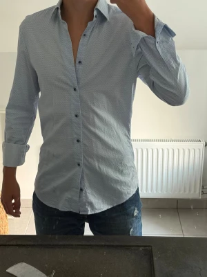 Ljusblå skjorta från Stenströms - Säljer en ljusblå skjorta från Stenströms med diskret geometriskt mönster. Skjortan har lång ärm, klassisk krage och knappar framtill. Perfekt till jeans eller chinos för en clean look.