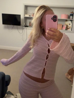 Rosa stickad loungewear-set - Mysigt rosa loungewear-set med långärmad topp och matchande byxor. Setet är stickat i ett mjukt material och toppen har stora knappar framtill samt vida ärmar. Perfekt för chill dagar hemma. Byxorna är uppsydda för att passa mig som är 161 cm. Tröjan har en liten blå fläck vid en av knapparna men inget man tänker på!