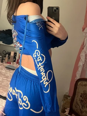Es hardy Blå jumpsuit med tryck och cut-outs mediun - Säljer en blå jumpsuit med vita grafiska tryck och coola cut-outs på sidorna. Långärmad modell med lös passform och resår i midjan. Materialet är troligtvis polyester eller liknande, vilket ger en sportig och bekväm känsla. Perfekt för dig som vill sticka ut med en unik stil. medium