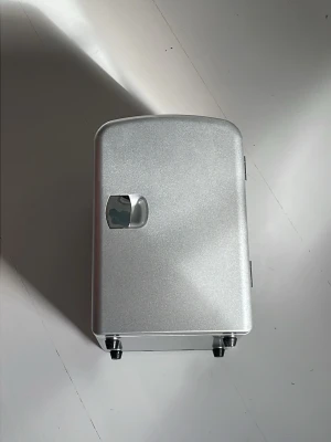 Snyggt silverfärgat sminkkylskåp - Stilrent sminkkylskåp i metallic silver med kompakt, rektangulär form och kromat handtag. Insidan är vit med ljusblå kylfack och tätslutande dörr. Perfekt för att hålla hudvård och smink fräscht. Tillverkad i plast och metall. Aldrig använd 