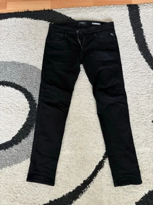 Svarta slim fit jeans från Replay - Snygga svarta slim fit jeans från Replay med klassisk femficksmodell och dragkedjegylf. Jeansen har en modern passform och är tillverkade i ett stretchigt material som ger skön komfort och stilren look.