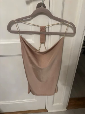 Beige satin linnetopp med strassdetalj - Säljer en beige linnetopp i satin med tunna axelband och snygg drapering både fram och bak. Toppen har en unik strassdetalj i ryggen som ger extra bling. Perfekt för dig som vill sticka ut lite extra!