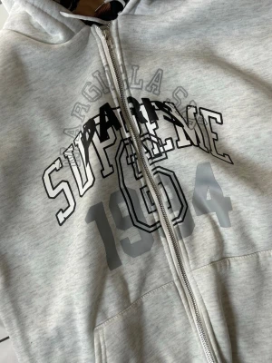 Grå zip hoodie med tryck - Säljer en ljusgrå hoodie med dragkedja  Huvan har ett unikt mönstrat innerfoder i färg. Hoodien har fickor framtill och ribbade muddar vid ärmar och nederkant. Perfekt för dig som gillar streetwear och vill sticka ut.