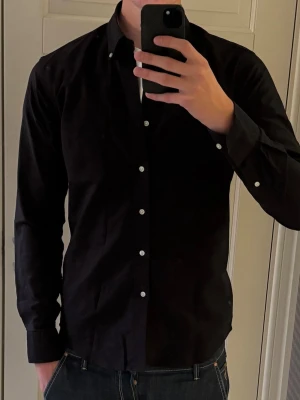 John Henric Skjorta - Stilren svart John Henric skjorta med vita eleganta knappar. Skönt material av bra kvalitet och fullt funktionell passform! Tokfräsch! 