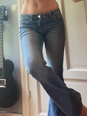 Blå bootcut jeans med utsvängda ben H&M - Säljer ett par blå bootcut jeans med klassisk femficksmodell och utsvängda ben. Jeansen har en snygg tvätt med lätt slitning framtill och normal midja. Perfekta för dig som gillar retrovibbar och vill ha ett par jeans som sticker ut lite extra.