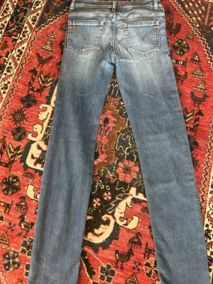 Blå raka jeans med broderade fickor från dondup  - Säljer ett par klassiska blå jeans med raka ben och snygga broderade detaljer på bakfickorna. Jeansen har normal midja och är tillverkade i ett mjukt denimtyg som ger en avslappnad look. Perfekta till vardags och lätta att matcha med olika stilar.