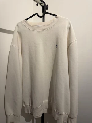 Vit sweatshirt från Polo Ralph Lauren - Klassisk vit sweatshirt från Polo Ralph Lauren med rund halsringning och broderad marinblå logga på bröstet. Tröjan har ribbade muddar vid ärmslut och nederkant. Perfekt för en clean och stilren look.