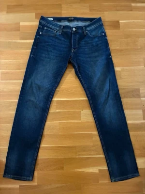 Mörkblå J&J jeans - Säljer ett par mörkblå jeans från Jack & Jones , som nya med klassisk femficksdesign och snygga slitningar. Jeansen har smal passform och kontrastsömmar, perfekta till en avslappnad stil. Storlek W34 L32