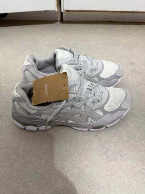 Vita och grå sneakers från Asics - Snygga sneakers från Asics i vitt och ljusgrått med mesh och syntetdetaljer. Skorna har en chunky sula och klassisk snörning. Perfekta för dig som gillar sportig och clean stil. St 45 men passar 44 utan konstigtheter 
