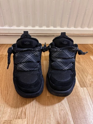 Ugg lowmels - Snygga svarta sneakers från UGG med grov sula och stickade detaljer. Skorna har ett unikt snörningssystem med breda, mönstrade snören och dragflikar bak. Använda men fortfarande i mycket fint skick! 