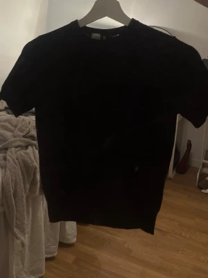 Svart t-shirt  - En stilren Svart stickad t-shirt med korta ärmar och rund hals. Tröjan har ribbade muddar vid ärmslut och nederkant, vilket ger en snygg passform. Perfekt för dig som gillar en enkel men trendig look.