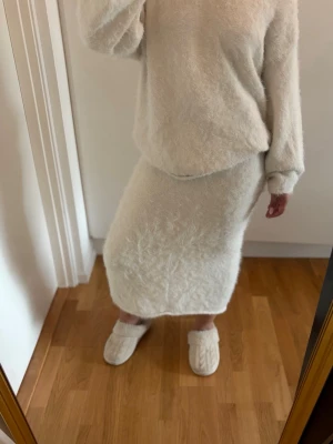 Ljus stickad långkjol - Mysig ljus långkjol i fluffigt stickat material. Kjolen har en rak passform och resår i midjan för extra komfort. Perfekt för dig som gillar en avslappnad och trendig stil.