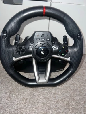 Svart racingratt till Xbox - Säljer en svart racingratt för Xbox med klassisk rund form och detaljer i silver. Ratten har gummerat grepp, flera knappar inklusive D-pad och triggers, Perfekt för racing- och bilspel. Använd väldigt sparsamt har använt väldigt lite.