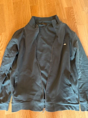 Mörkgrå stickad fullzip tröja från Loro  - Snygg mörkgrå stickad ziptröja från Loro. Tröjan har hög krage, dragkedja framtill och två fickor på sidorna. Materialet är mjukt och har en diskret struktur. Perfekt för lager på lager och enkel att matcha.