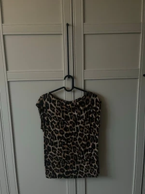 Leopardmönstrad topp med kort ärm - Snygg topp med leopardmönster i beige, brunt och svart. Modellen har korta ärmar och rund halsringning. Perfekt för dig som vill sticka ut med ett djurmönster. Materialet känns mjukt och följsamt mot huden.