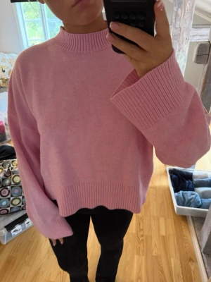 Oversized rosa stickad tröja - Säljer en oversized stickad tröja i ljusrosa med breda ärmar och ribbade muddar vid hals, ärmslut och nederkant. Tröjan har en högre rund halsringning och avslappnad passform, perfekt för en chill och trendig look.