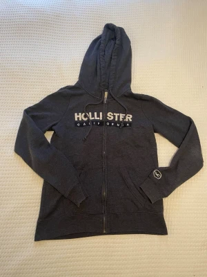 Hollister hoodie  - Sjukt snygg Hollister Zip hoodie i storlek S. Den passar snarare XS än S. Hoodien har slitningar på armbågarna och har blivit lite vitt, det syns på bild