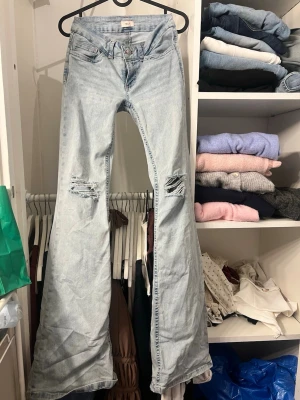 Ljusblå bootcut jeans med slitningar - Säljer ett par ljusblå bootcut jeans med slitningar på båda knäna och broderade detaljer på bakfickorna low waist💗