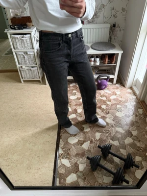 Svarta raka jeans från Zara - Säljer ett par svarta jeans med rak passform och hög midja. Jeansen har klassiska fem fickor och stängs med knapp och dragkedja. Materialet är denim i bomull och de har en avslappnad look som passar till det mesta.