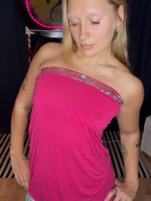 Rosa tubtopp med paljettdetalj - Snygg rosa tubtopp med glittrande paljetter längs överkanten. Toppen är axelbandslös och har en bandeauformad passning som sitter bekvämt. Perfekt för dig som vill sticka ut lite extra med en färgstark och trendig look.