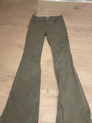 Khakigröna bootcut jeans från 157 - Snygga khakigröna jeans från 157 med bootcut-modell och är låg midja. Jeansen har klassiska fem fickor och stängs med knapp och dragkedja. Perfekta för dig som gillar retrovibbar och vill ha ett par unika byxor i garderoben.