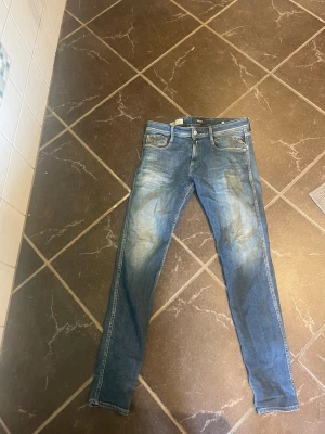 Blå slim fit jeans med slitningar - Säljer ett par blå slim fit jeans med snygga slitningar och tvättade detaljer. Jeansen har fem fickor, normal midja och klassisk knappgylf. Passar perfekt till en avslappnad och trendig stil.