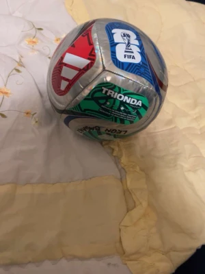 Färgglad fotboll från Trionda - Säljer en fotboll från Trionda med färgglada paneler i rött, blått, grönt och silver. Bollen har FIFA-logga och tydliga mönster på ytan. Perfekt för träning eller spontanspel med vänner.
