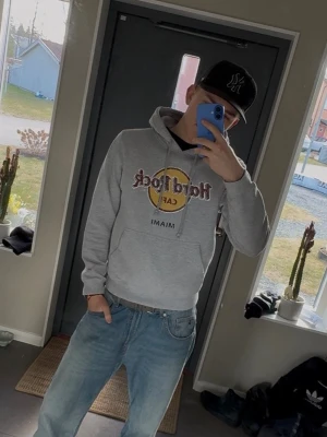 Grå Hard Rock Cafe hoodie Miami - Säljer en grå hoodie från Hard Rock Cafe med klassisk logga i gult och rött samt texten 'Miami' under. Hoodien har huva med dragsko och en stor magficka. Perfekt för dig som gillar streetwear och vill ha en chill look.