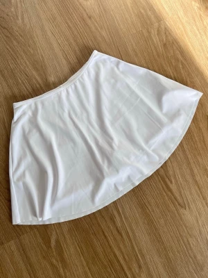 Vit minikjol med shorts från Cotton on Body - Säljer en vit minikjol i tränings-material med inbyggda shorts. Shortsen har två fickor, en på vardera sidor, för mobil, nycklar mm. Använd en gång.   Köpt hos Cotton on Body i Australien.