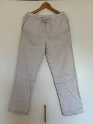 Beiga linne/bomullsbyxor med dragsko storlek XS från H&M - Snygga och luftiga linne/ bomullsbyxor i beige med rak passformoch elastisk midja med dragsko. Byxorna har sidofickor och en bakficka. Perfekt skick! Storlek XS från H&M