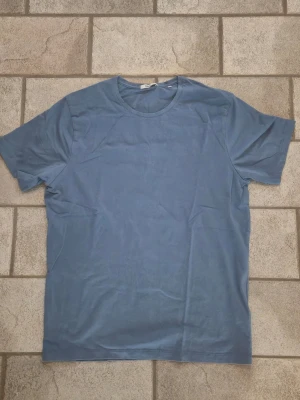 Blå basic t-shirt från Bläck - En enkel blå t-shirt från Bläck i storlek L. T-shirten har rund halsringning och korta ärmar. Tillverkad i mjuk bomull som känns skön mot huden. Perfekt till jeans eller shorts för en avslappnad look.