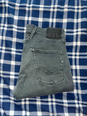 Replay Anbass jeans  - Snygga mörkgrå jeans i slim fit-modell med klassiska fem fickor och diskreta sömmar på bakfickan. Jeansen har bälteshällor och knappgylf. Perfekta för en trendig och avslappnad stil. Obs notera bilden där det finns en pytteliten fläck ! JAG SKICKAR EJ FLER BILDER NÄR JAG BÄR JEANSEN! för bättre inblick i passformen rekommenderar jag att googla på modellnamnet. För storleksguide kolla måtten noggrant då jeansen alltid kan vara uppsydda heller krympta och jag ej tar emot returer :) 