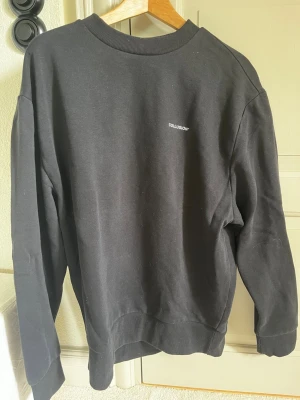 Svart sweatshirt från COLLUSION - Svart sweatshirt från COLLUSION med enkel och clean design. Tröjan har rund halsringning, ribbade muddar och en liten vit logga på bröstet. Perfekt för en avslappnad och stilren look.