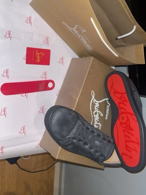 Svarta sneakers från Christian Louboutin - Snygga svarta sneakers från Christian Louboutin i mocka med klassisk röd sula och gulddetaljer på insidan. Skorna har lågt skaft, svarta skosnören och diskret logga på sidan. Perfekta för dig som vill ha en exklusiv och stilren look.
