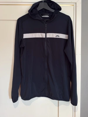 J.Lindeberg zip hoddie - Säljer en mörkblå zip i storlek L från J.Lindeberg. Tillverkad i ett tunt, stretchigt material som känns sportigt och modernt. Tröjan är både bekväm och snygg i en slim passform, passar perfekt till t,ex golfbanan. Nypris cirka 1500kr, bara använd fåtal gånger.