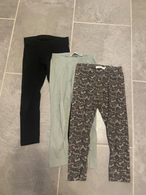 3-pack leggings i olika färger - Säljer ett 3-pack leggings i stretchigt material. Ett par är helsvarta, ett par ljusgrå och ett par mörkgrå med färgglatt textmönster där det står bland annat 'Cute' och 'Rock'. Perfekta för en avslappnad och bekväm stil.