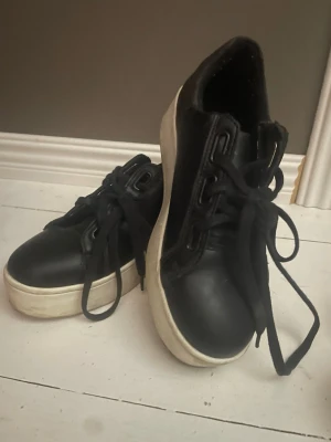 Svarta skor - Snygga svarta sneakers med tjock vit platåsula och svarta skosnören. Skorna har en clean design i slätt material och passar perfekt till streetwear eller casual outfits. Klassisk låg modell som är enkel att matcha.