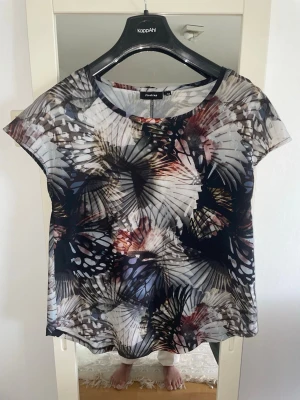 Mönstrad blus från Firetrap - Säljer en luftig blus från Firetrap med abstrakt mönster i svart, beige, grått och inslag av rött. Blusen har rund halsringning och korta ärmar. Perfekt för dig som gillar unika prints och en avslappnad passform.