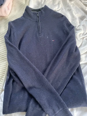 Mörkblå halvzip stickad tröja Tommy Hilfiger  - Mörkblå stickad tröja från Tommy Hilfiger med halv dragkedja och liten broderad logga på bröstet. Tröjan har ribbad krage, muddar och nederkant. Perfekt för lager på lager och enkel att matcha med jeans eller kjol.