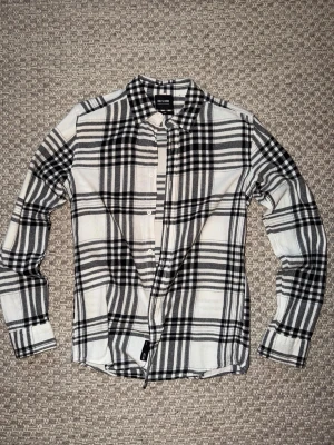 Svartvit rutig skjorta Only & Sons - Säljer en svartvit rutig skjorta från Only & Sons. Skjortan har klassisk krage, knappar framtill och långa ärmar. Perfekt för dig som gillar en stilren och tidlös look. Materialet känns mjukt och bekvämt mot huden.